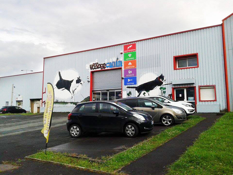 La façade du Village Canin, décorée de fresques de chiens en action, avec son parking